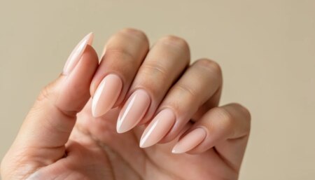 Mão feminina com unhas delicadas translúcidas em nude rosado, formato amendoado e brilho natural